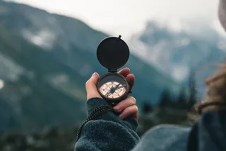 Nahaufnahme einer Hand, die einen Kompass hält, mit einem unscharfen Bergpanorama im Hintergrund
